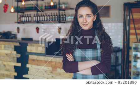 Portrait of attractive confident young woman small business owner standing in her opening coffee shop and smiling looking at camera. Coffee house interior in background. Portrait of attractive confident young woman small business owner standing in her opening coffee shop and smiling looking at camera. Coffee house interior in background. 95201890