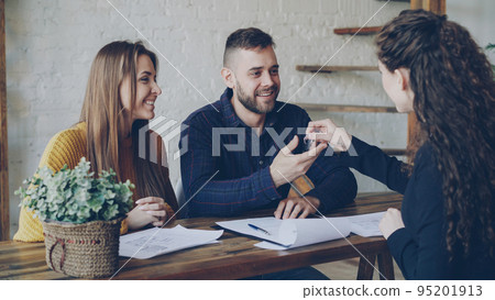 Loving couple is purchasing house signing sales agreement with housing agent, getting key after making deal with realtor. Buying real estate concept. Loving couple is purchasing house signing sales agreement with housing agent, getting key after making deal with realtor. Buying real estate concept. 95201913