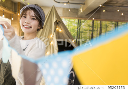 A young woman decorating with a garland at a house camp. 95203153