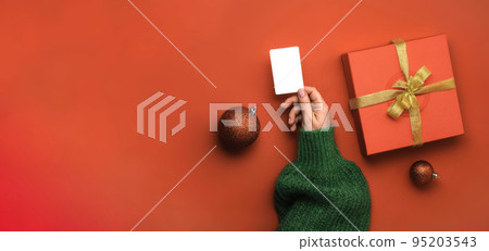 Christmas shopping concept. Flat lie hands in a green sweater with credit card. Banner on a red background Christmas shopping concept. Flat lie hands in a green sweater with credit card. Banner on a red background 95203543