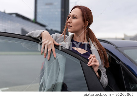 A business woman stands next to an open car door against the backdrop of a business center A business woman stands next to an open car door against the backdrop of a business center 95203865