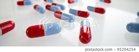 Lot of blue and red capsules lying on white table closeup background 95204254