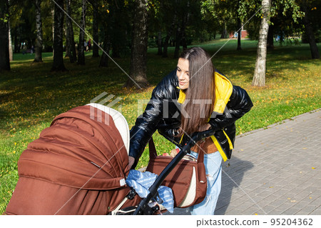 A young woman looks into a stroller and smiles A young woman looks into a stroller and smiles 95204362