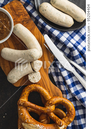 Traditional Bavarian white sausages on cutting board and pretzels. Traditional Bavarian white sausages on cutting board and pretzels. 95204404