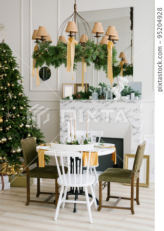 Stylish festive Christmas table with vintage chairs near the marble fireplace and Christmas tree in the living room or dining room in the house 95204928