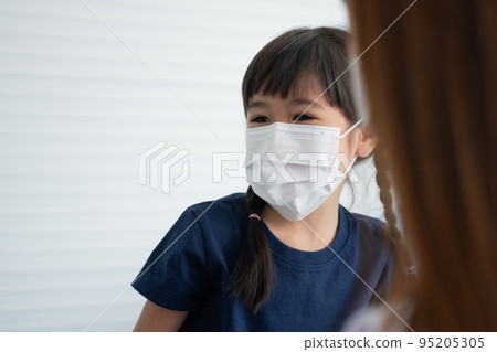 Asian parents wear face masks to little daughter for protection against coronavirus covid 19 before going to school. Mom teaches daughter to put on a medical mask 95205305