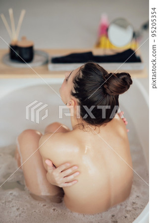 Young woman embracing herself taking a bath view from the back Young woman embracing herself taking a bath view from the back 95205354