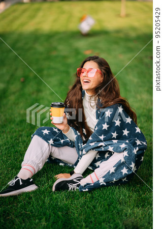 Young woman with a paper glass of coffee sitting on the grass 95205429