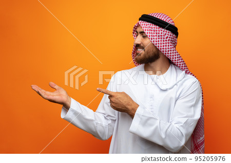 Young Arab man pointing hand to copy space on orange background Young Arab man pointing hand to copy space on orange background 95205976