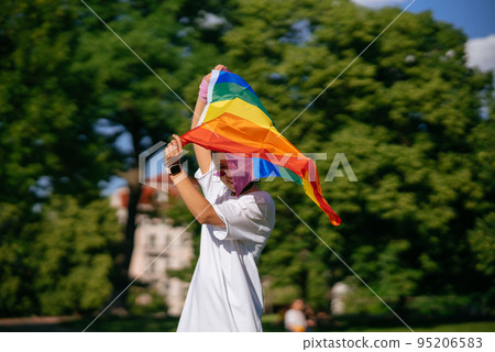 Young woman waving LGBT pride flag in the park. 95206583