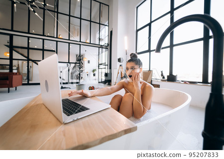 Young woman working on laptop while taking a bathtub 95207833