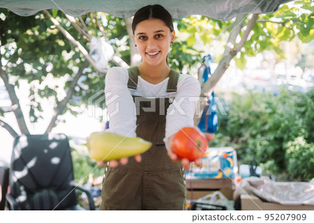Young saleswoman holding bell pepper and tomato in hands 95207909