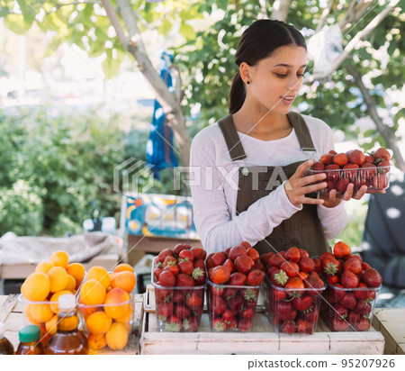 Young positive saleswoman at work, holding strawberries in her hands Young positive saleswoman at work, holding strawberries in her hands 95207926