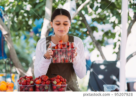 Young positive saleswoman at work, holding strawberries in her hands Young positive saleswoman at work, holding strawberries in her hands 95207928