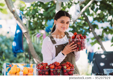 Young positive saleswoman at work, holding strawberries in her hands 95207929