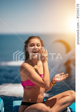 Smiling woman is applying sunscreen on her face. 95208176
