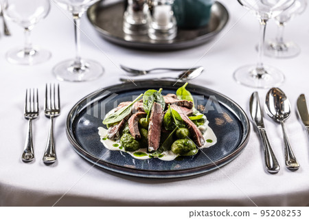 Creatively cooked beef flank steak with spinach gnocchi served on a ceremonially prepared table in the hotel restaurant Creatively cooked beef flank steak with spinach gnocchi served on a ceremonially prepared table in the hotel restaurant 95208253