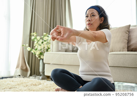 Healthy Asian-aged woman stretching her hands, practicing yoga in her home living room. 95208756