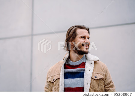 Smiling male model looking at the distance while posing over the blank wall Smiling male model looking at the distance while posing over the blank wall 95208907