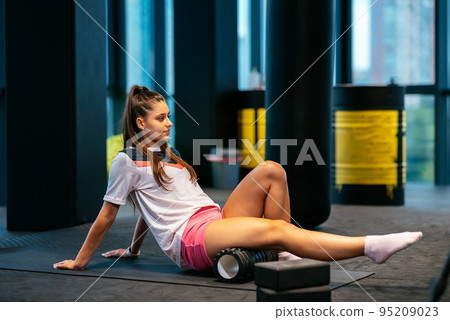 Young woman using a foam roller while doing stretching exercises Young woman using a foam roller while doing stretching exercises 95209023