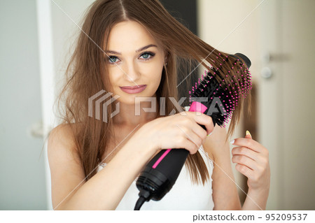 Woman straightening hair with straightener comb at home 95209537