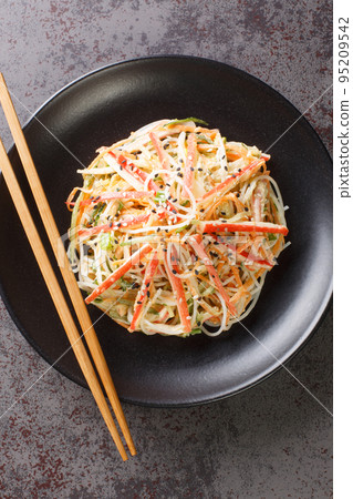 Japanese kani salad with crab sticks, glass vermicelli, carrot, cucumber and sesame seeds dressed with mayonnaise close-up in a plate. vertical top view Japanese kani salad with crab sticks, glass vermicelli, carrot, cucumber and sesame seeds dressed with mayonnaise close-up in a plate. vertical top view 95209542