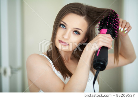 Woman drying long hair with hair dryer round brush. 95209557