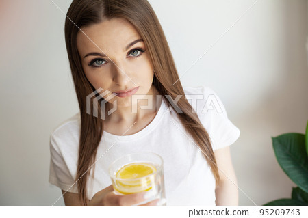 Beautiful young woman drinking fresh water with lemon at home Beautiful young woman drinking fresh water with lemon at home 95209743