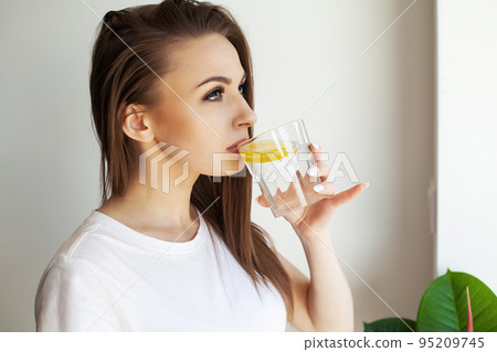 Beautiful young woman drinking fresh water with lemon at home Beautiful young woman drinking fresh water with lemon at home 95209745