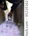 A person wearing a helmet taking a picture of the cherry blossoms in the gutter 95210162