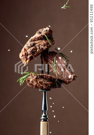 Beef steak on a fork sprinkled with rosemary and sea salt. 95211498