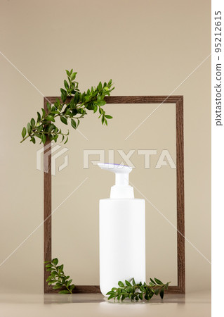 White cosmetic bottle , stands in an empty wooden frame with branches of a green plant White cosmetic bottle , stands in an empty wooden frame with branches of a green plant 95212615