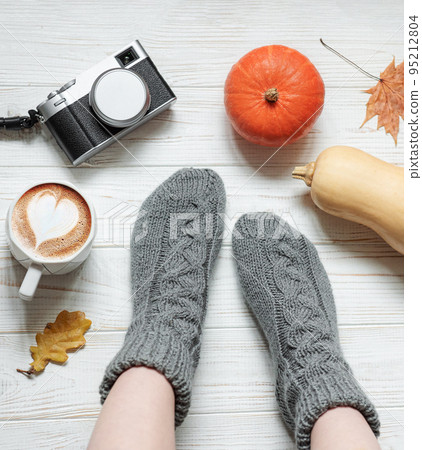 Legs of a girl in knitted socks on a wooden background next to pumpkins and autumn leaves Legs of a girl in knitted socks on a wooden background next to pumpkins and autumn leaves 95212804