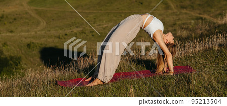 Young Woman Doing Bridge Exercise During Yoga Practice Outdoors with Beautiful Background Young Woman Doing Bridge Exercise During Yoga Practice Outdoors with Beautiful Background 95213504