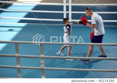 Two athletes, son and father is doing sports in gym. Beginner boxer workout with his coach ar boxing ring, indoors. Sport, power, energy and active lifestyle Two athletes, son and father is doing sports in gym. Beginner boxer workout with his coach ar boxing ring, indoors. Sport, power, energy and active lifestyle 95214180