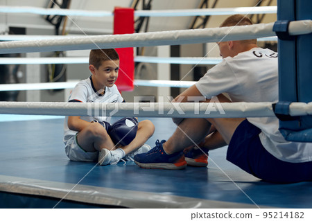 Two athletes, son and father is doing sports in gym. Beginner boxer workout with his coach ar boxing ring, indoors. Sport, power, energy and active lifestyle Two athletes, son and father is doing sports in gym. Beginner boxer workout with his coach ar boxing ring, indoors. Sport, power, energy and active lifestyle 95214182