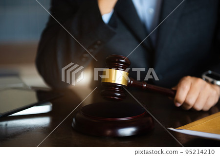 Close up view of auction hammer on the desk in lawyer office and lawyer writing document as courtroom. Close up view of auction hammer on the desk in lawyer office and lawyer writing document as courtroom. 95214210