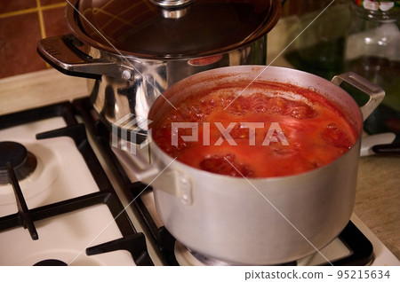 Close-up of tomato juice boiling in metal saucepan on the stove. Preparing homemade passata from organic ripe harvested juicy tomatoes, according to Italian traditional recipe. Canning food for winter Close-up of tomato juice boiling in metal saucepan on the stove. Preparing homemade passata from organic ripe harvested juicy tomatoes, according to Italian traditional recipe. Canning food for winter 95215634