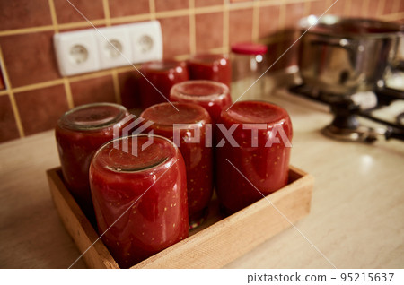 Still life with sterilized tins of freshly brewed tomato sauce, passata or juice, upside down on a wooden crate. Canning organic homegrown vegetables for the winter. Making preserves. Conservation Still life with sterilized tins of freshly brewed tomato sauce, passata or juice, upside down on a wooden crate. Canning organic homegrown vegetables for the winter. Making preserves. Conservation 95215637