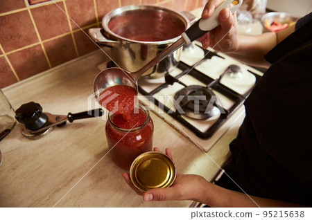 Top view of a housewife pouring freshly boiled tomato juice into a sterilized jar, preparing homemade organic passata or sauce. Preserving, canning or marinating food for the winter Top view of a housewife pouring freshly boiled tomato juice into a sterilized jar, preparing homemade organic passata or sauce. Preserving, canning or marinating food for the winter 95215638