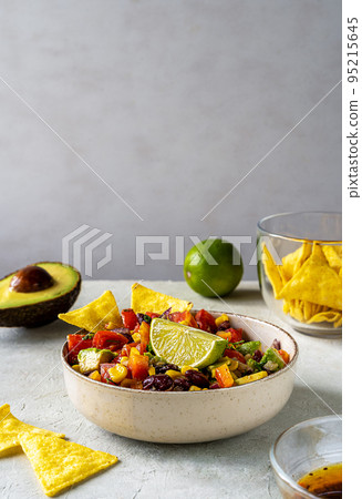 Cowboy caviar is traditional Mexican vegetable salad in bowl with ingredients and nachos on grey background Cowboy caviar is traditional Mexican vegetable salad in bowl with ingredients and nachos on grey background 95215645