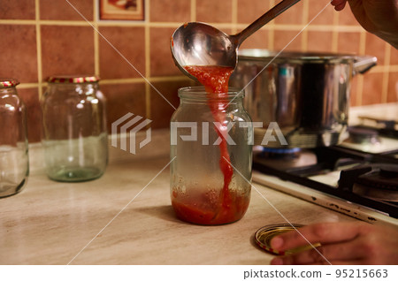 Close-up cooking, canning homemade passata from organic ripe juicy tomatoes for the winter. Canning food. Making preserves. Conservation. Housewife pouring boiling tomato juice into a sterilized jar Close-up cooking, canning homemade passata from organic ripe juicy tomatoes for the winter. Canning food. Making preserves. Conservation. Housewife pouring boiling tomato juice into a sterilized jar 95215663