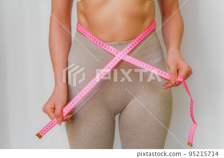 Close up of slim woman measuring her waist's size with tape measure. Isolated on white background. 95215714