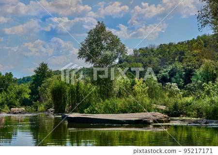Calm view with a quiet backwater of the river with large stones and dense forest 95217171