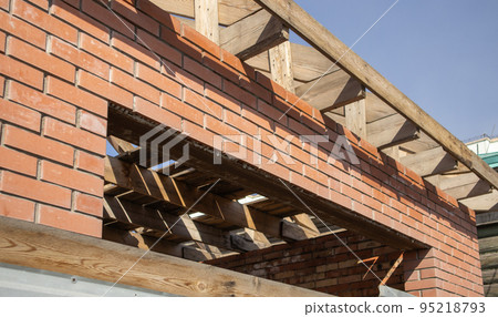 A private residential building under construction with a wooden frame roof structure. Unfinished brick building under construction, close-up 95218793