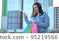 The girl after shopping holds a cash receipt in her hands and looks at the prices of goods. Woman with colored paper bags 95219566