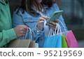 two girlfriends with colored bags after shopping look at the phone and share photos with purchases in social networks 95219569