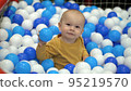 One year old boy sits in a pool with colorful plastic balls and plays with them 95219570