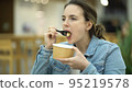 Woman at food court eating caesar salad from paper utensils. Business lady taking a lunch break 95219578