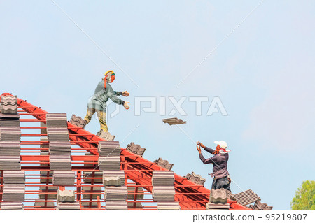 Construction roofer installing roof tiles at house building site Construction roofer installing roof tiles at house building site 95219807